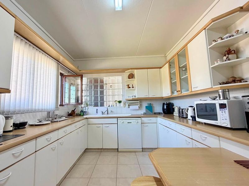 A functional U-shaped kitchen featuring white cabinetry, laminate countertops, ceramic tile flooring, and a unique glass block window for natural light.