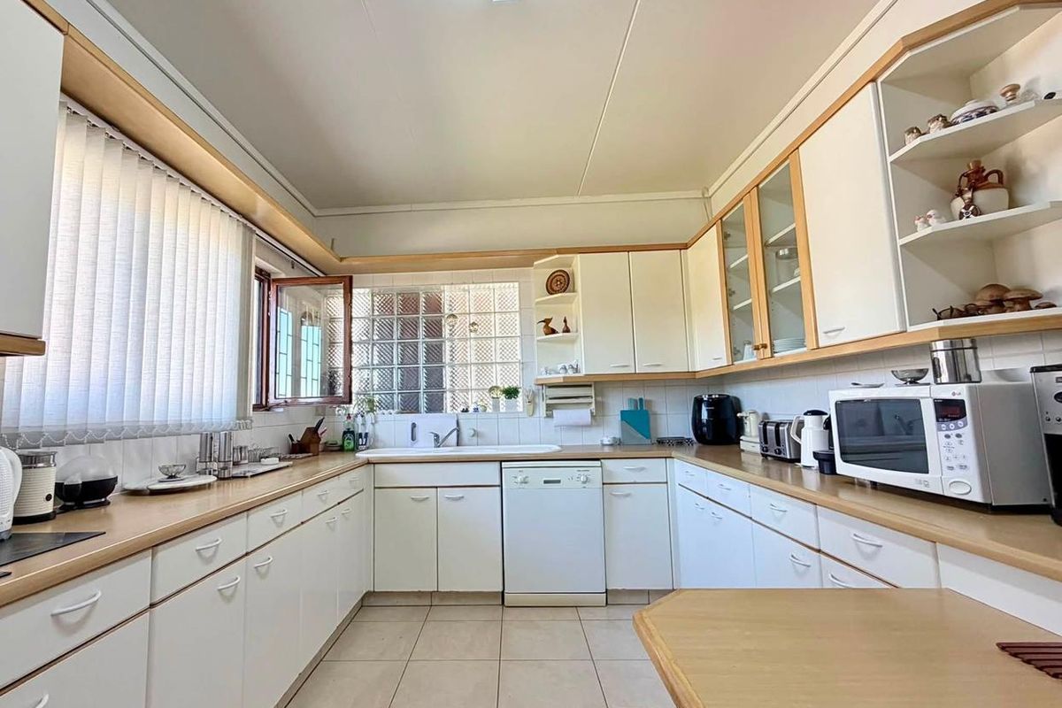 A functional U-shaped kitchen featuring white cabinetry, laminate countertops, ceramic tile flooring, and a unique glass block window for natural light.