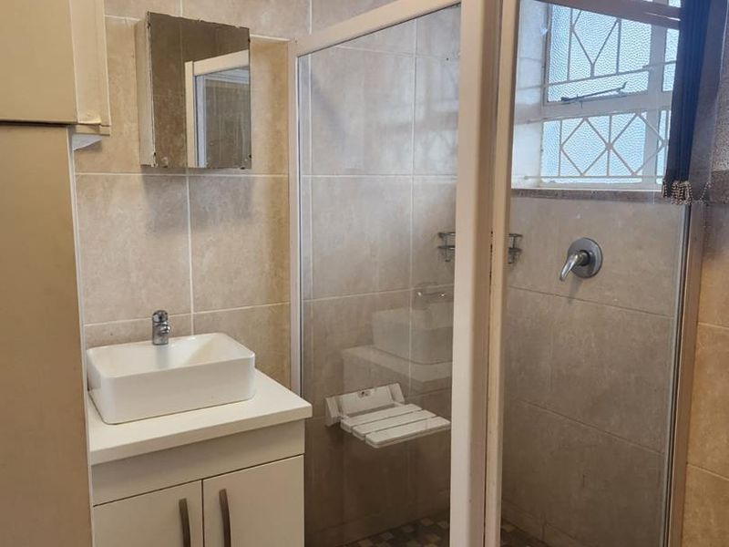 A functional bathroom featuring a shower enclosure, vanity cabinet with vessel sink, and neutral wall tiling.