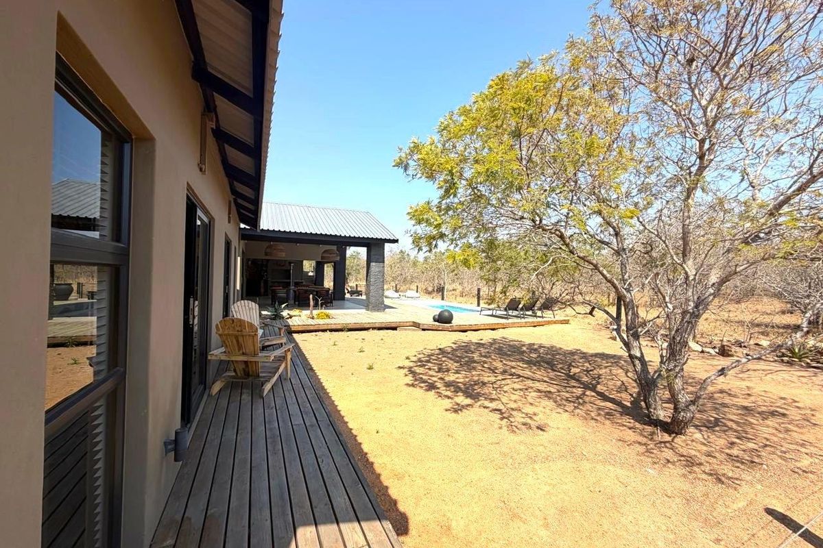Rear view of the property featuring a wooden deck, covered patio area, and a swimming pool set within a natural landscape.