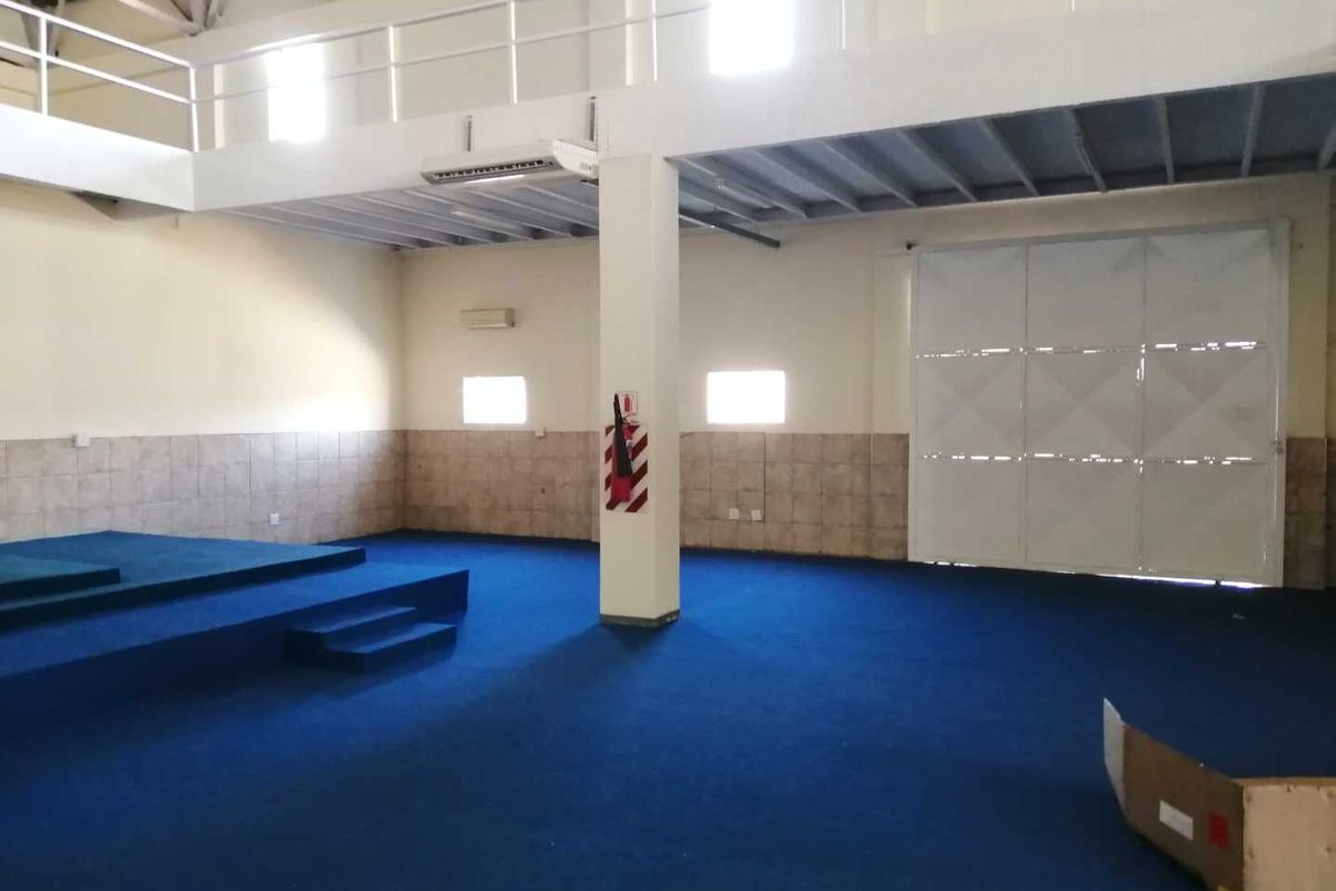 Spacious industrial utility area featuring a mezzanine level, high ceilings with exposed structure, tiled wainscoting, and a large roller door for easy access.