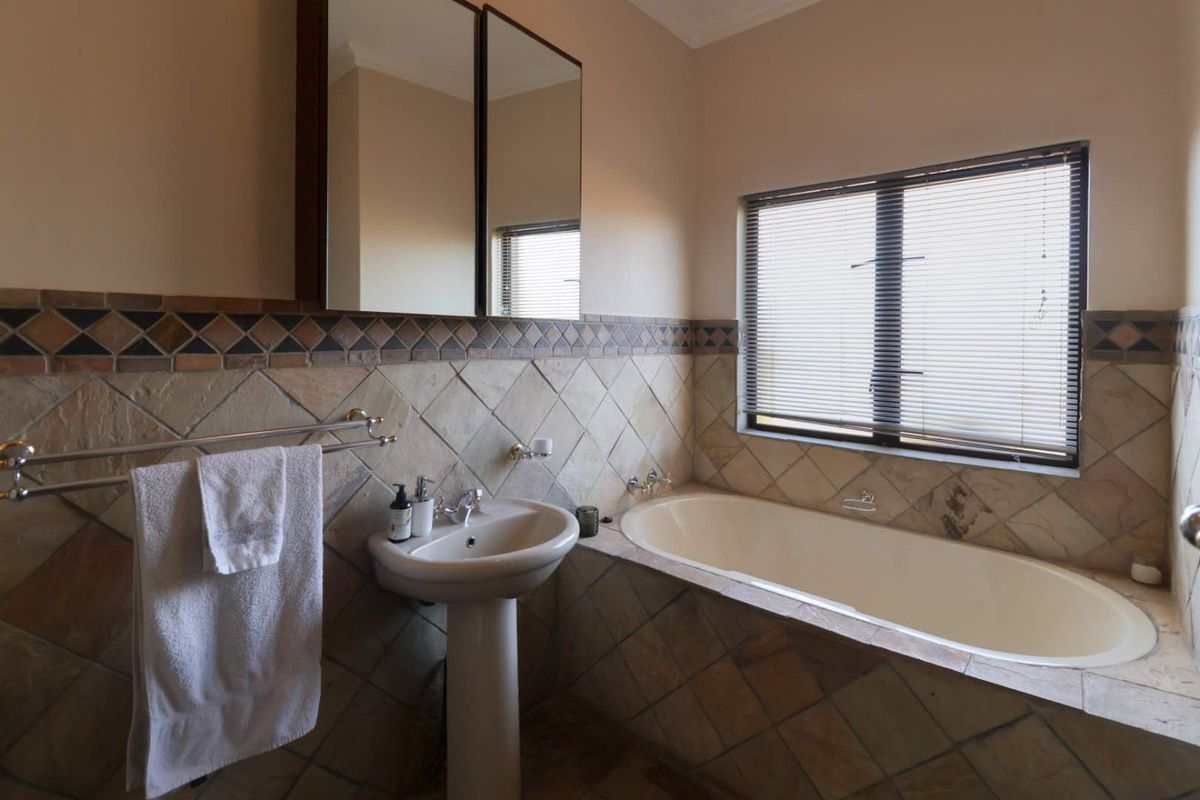A bathroom featuring a built-in bathtub, pedestal basin, and mirrored medicine cabinet with natural stone wall tiling.