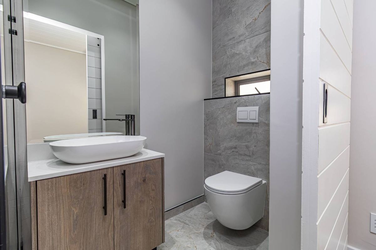 Modern bathroom featuring a wall-mounted toilet, sleek vanity cabinet with a vessel sink, and contemporary grey tiled finishes.