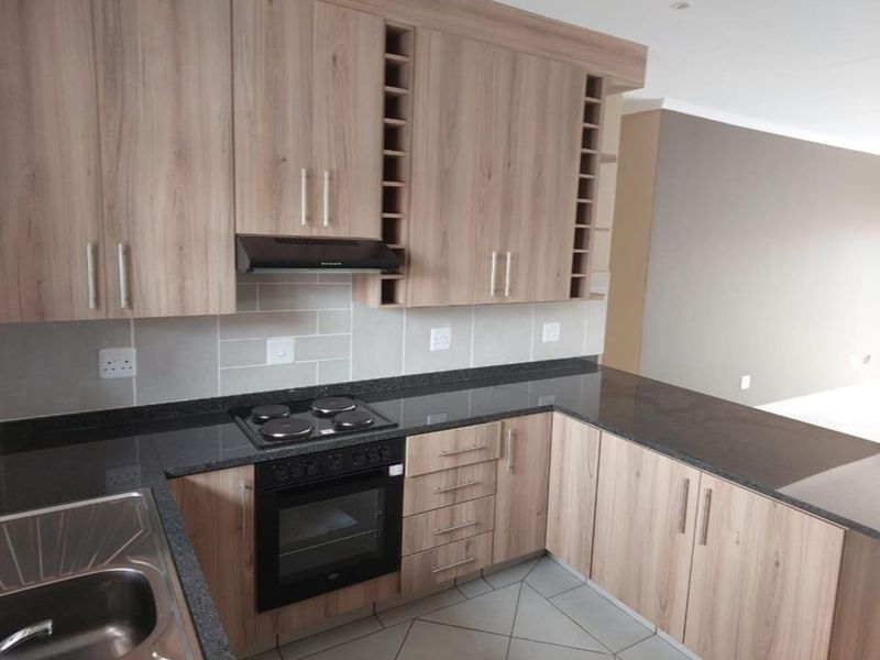 Modern kitchen featuring light wood-finish cabinetry, dark granite countertops, integrated electric hob and oven, and a clean tiled backsplash.