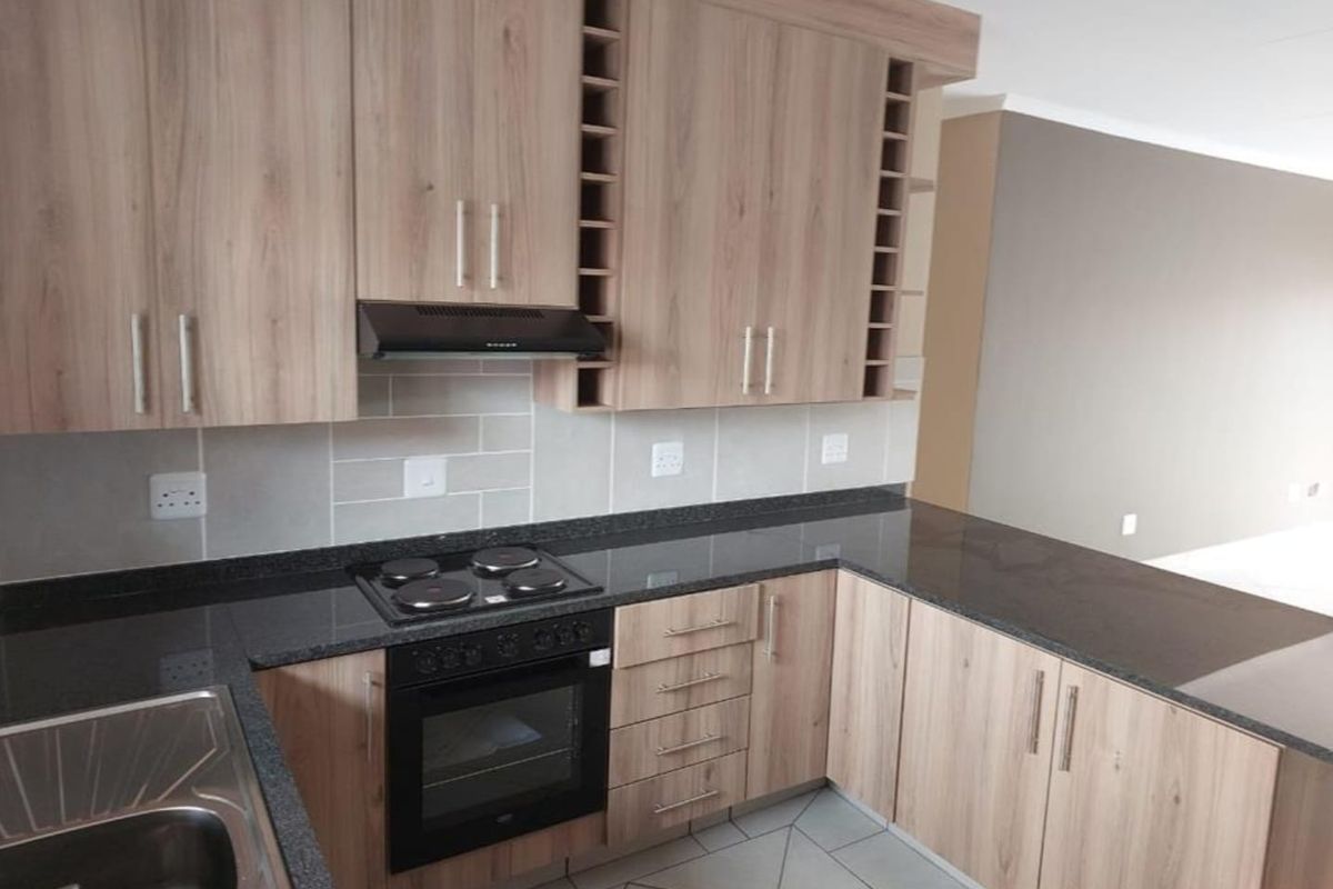 Modern kitchen featuring light wood-finish cabinetry, dark granite countertops, integrated electric hob and oven, and a clean tiled backsplash.