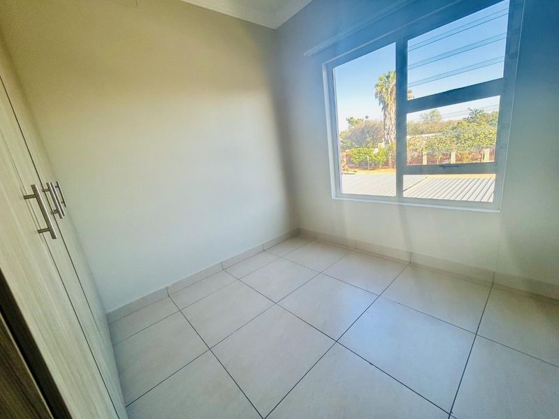 A bright, empty bedroom featuring neutral tiled flooring and built-in cupboards, offering a clean and versatile space ready for personalization.