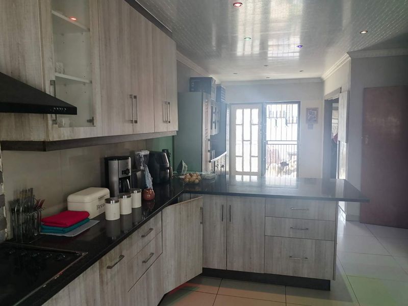 A functional kitchen featuring light wood-grain cabinetry, dark granite countertops, integrated hob, and tiled flooring with direct access to an outdoor area.