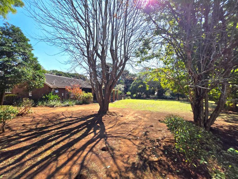 A view of the rear garden featuring a spacious lawn, mature trees, and a brick-built house with a tiled roof.