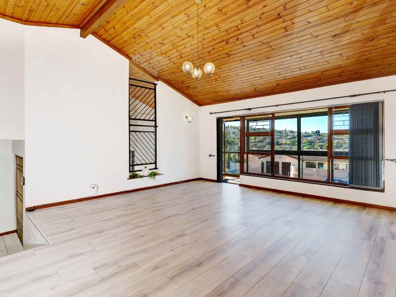 Spacious living area featuring a high vaulted timber ceiling, modern laminate flooring, and large windows offering expansive views.