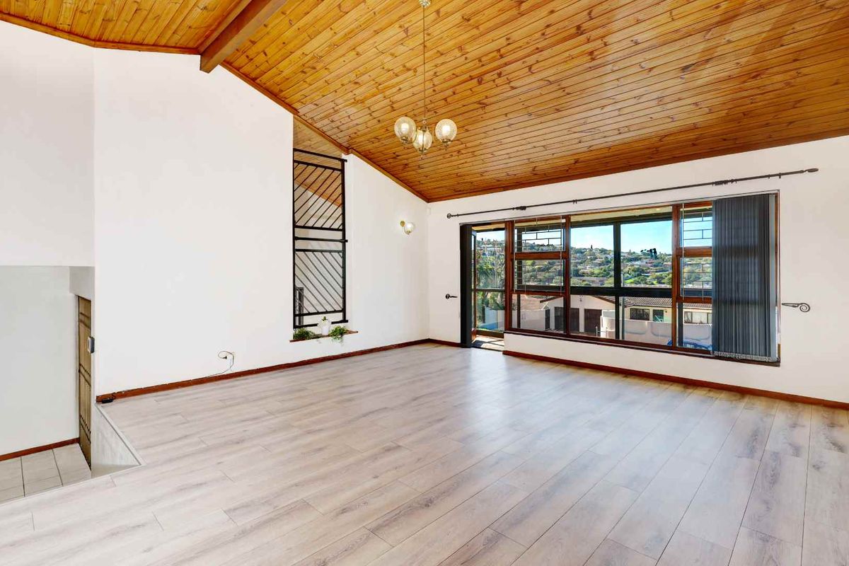 Spacious living area featuring a high vaulted timber ceiling, modern laminate flooring, and large windows offering expansive views.
