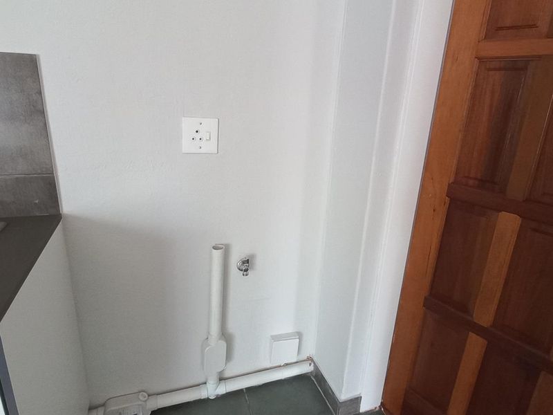 A functional laundry area featuring a stainless steel sink, tiled splashback, and dedicated plumbing connections for a washing machine.