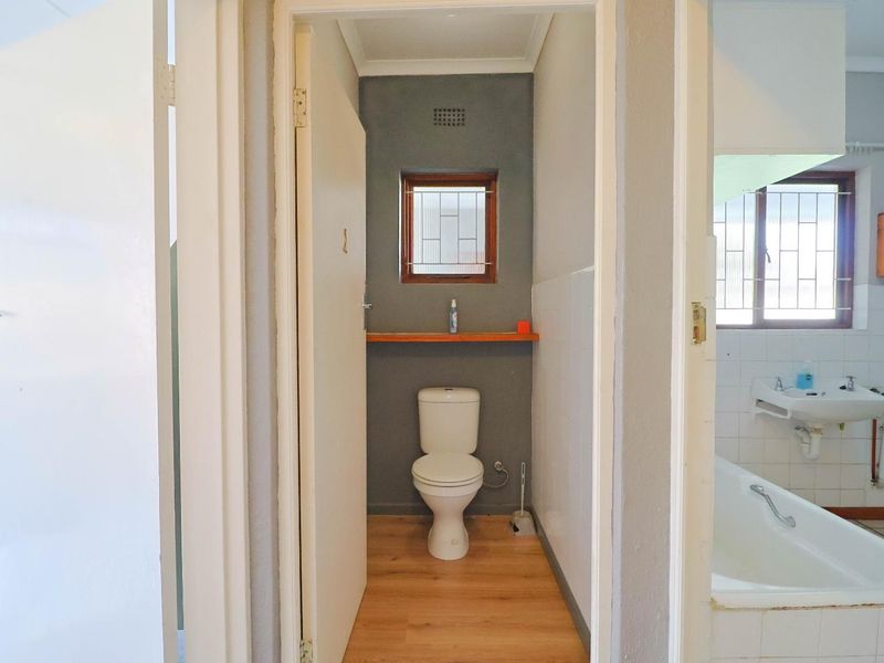 A functional bathroom featuring a separate toilet cubicle, a bathtub, and a pedestal basin with tiled splashbacks and security bars on the windows.