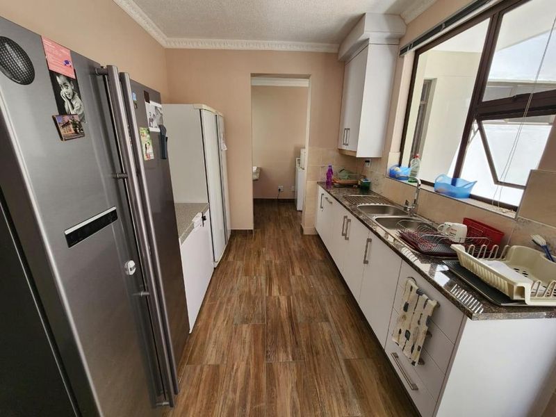 A functional kitchen featuring granite countertops, built-in cabinetry, and a stainless steel double sink with tiled flooring and classic cornice detailing.