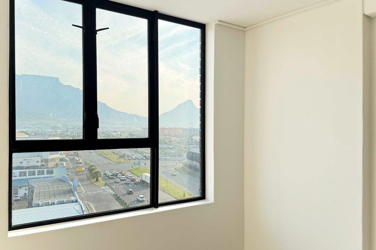 A bright, empty bedroom featuring a large window with black aluminium frames and expansive mountain and city views.