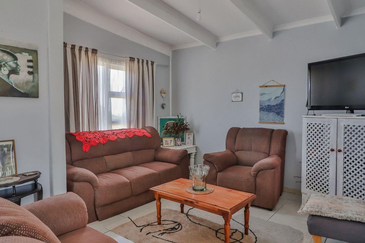 A comfortable living room featuring exposed ceiling beams, tiled flooring, and large windows that provide natural light to the space.