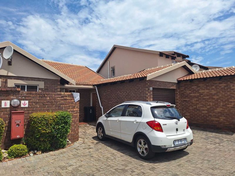Front exterior view of a townhouse featuring a brick facade, tiled roof, and a paved driveway leading to a garage.