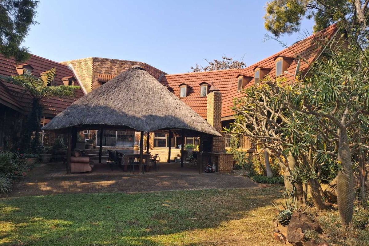Spacious rear garden featuring a large thatched lapa with a built-in braai, set against a traditional facebrick farmhouse with clay tile roofing.