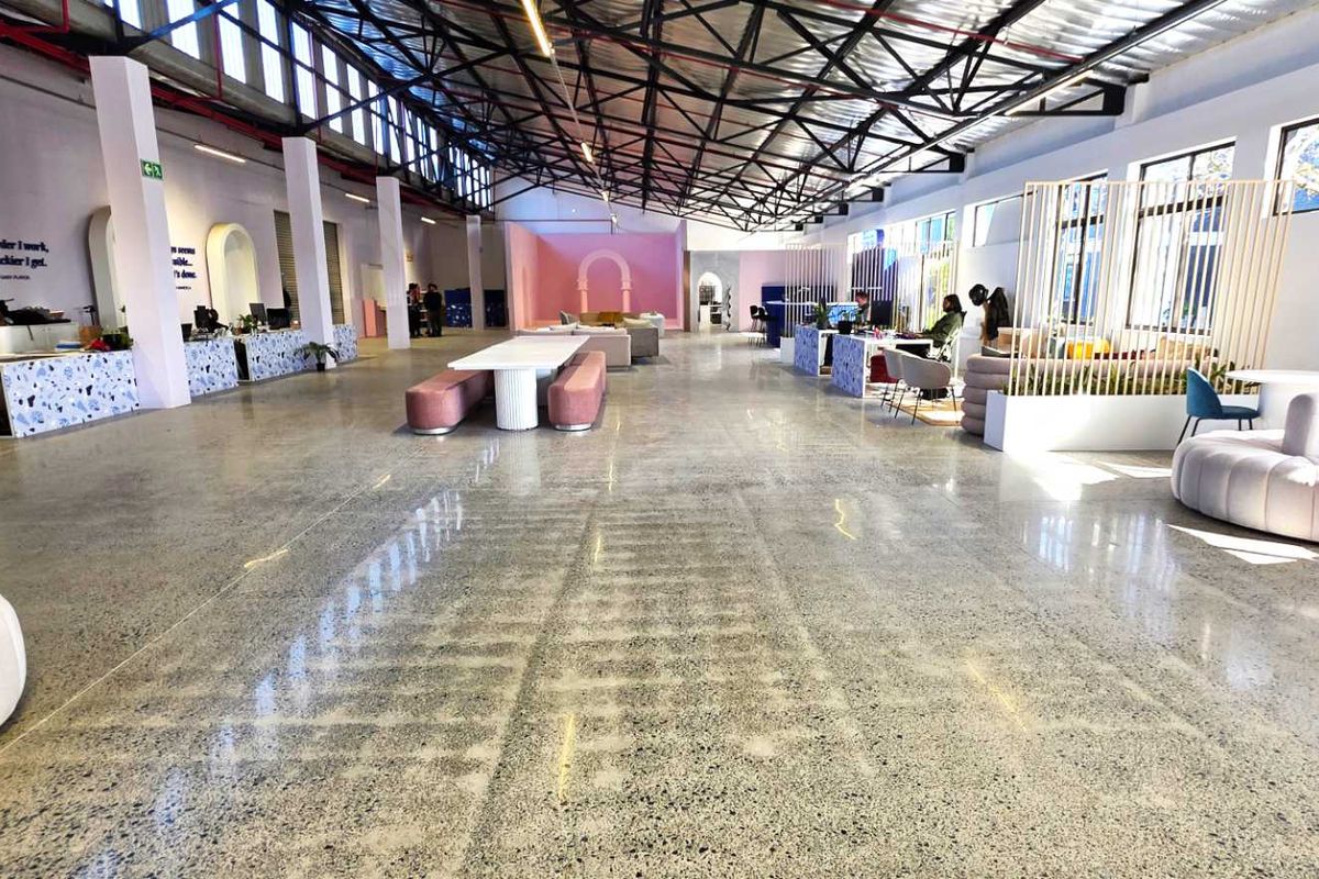 Spacious open-plan industrial office area featuring polished concrete floors, high exposed steel roof trusses, and abundant natural light from clerestory windows.