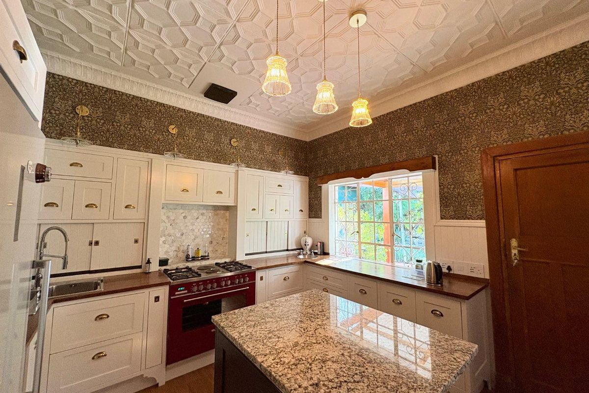 A character-filled kitchen featuring white cabinetry, granite countertops, a red range cooker, patterned wallpaper, and a decorative pressed metal ceiling.