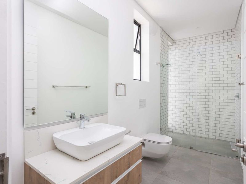 Modern bathroom featuring a vessel sink on a stone-topped vanity, wall-mounted toilet, and a spacious walk-in shower with subway tile finishes.