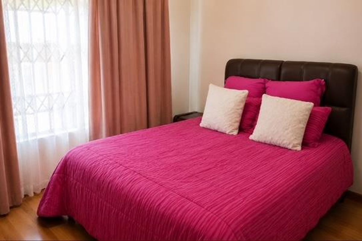 A functional bedroom featuring laminate flooring and a window fitted with a security gate.