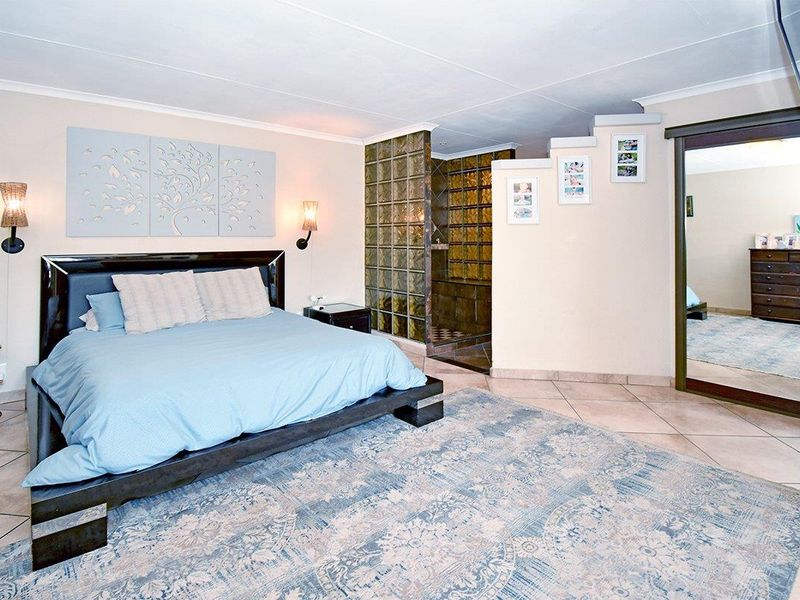Spacious bedroom featuring tiled flooring, a glass block partition separating the ensuite area, and a large built-in mirror.