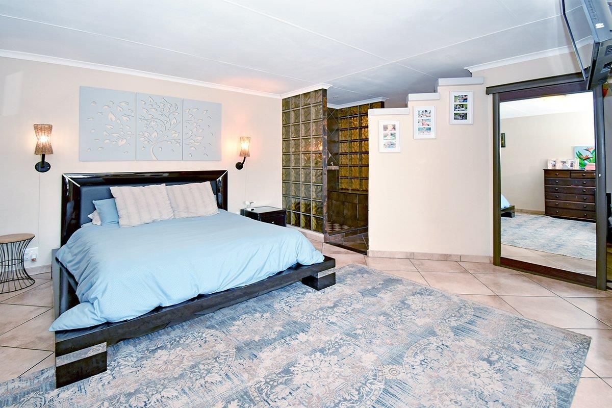 Spacious bedroom featuring tiled flooring, a glass block partition separating the ensuite area, and a large built-in mirror.