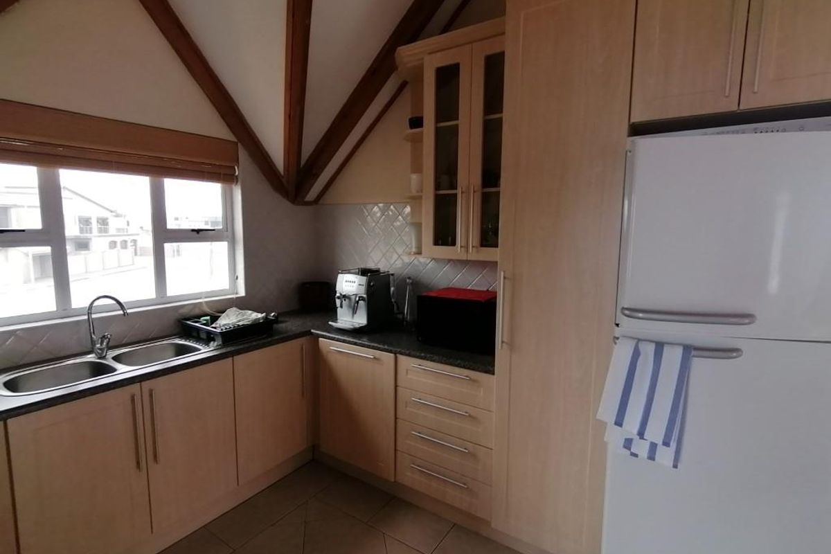 A functional kitchen featuring light wood cabinetry, tiled flooring, a double basin sink, and exposed timber ceiling beams.