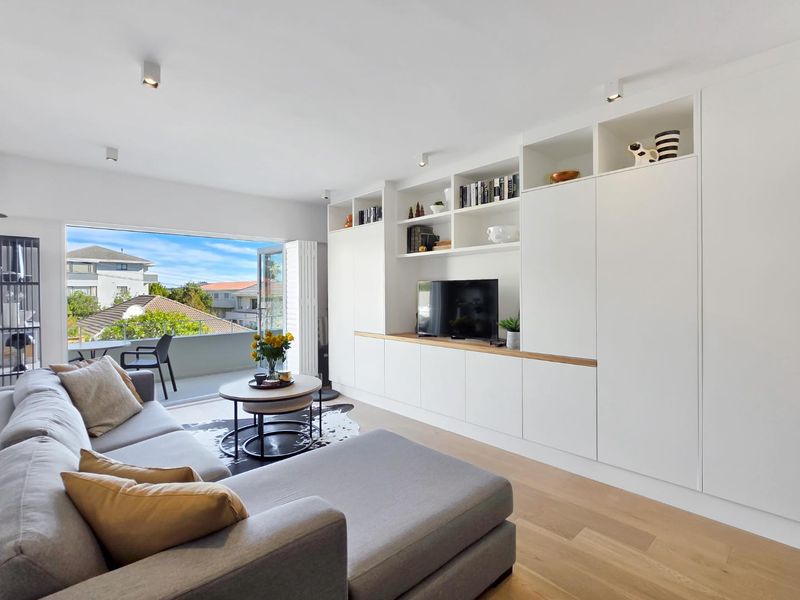 Modern living room featuring extensive built-in white cabinetry, hardwood flooring, and large sliding doors opening onto a private balcony.