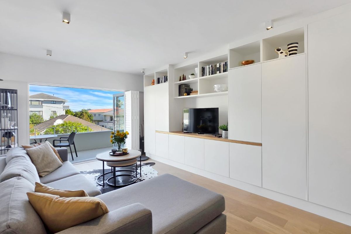 Modern living room featuring extensive built-in white cabinetry, hardwood flooring, and large sliding doors opening onto a private balcony.