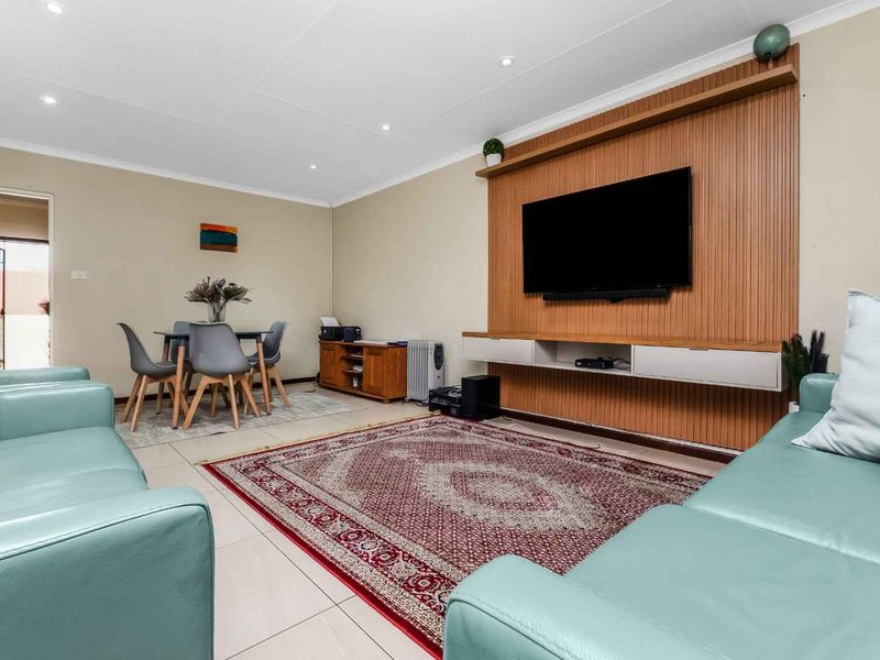 A well-maintained living room featuring tiled flooring, recessed downlights, and a modern built-in media wall unit with timber-look paneling.