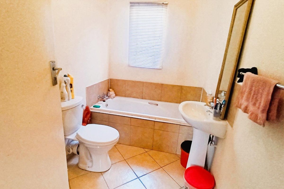 A functional bathroom featuring a built-in bathtub with tiled surround, a pedestal basin, and a standard toilet.