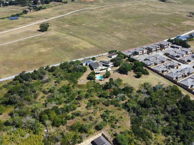An aerial view of a residential property featuring a swimming pool, surrounded by natural vegetation and adjacent to a residential estate.