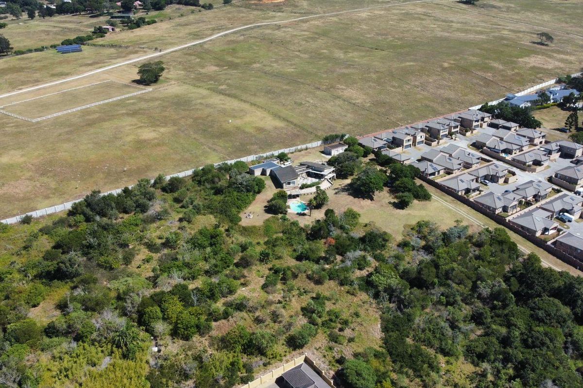 An aerial view of a residential property featuring a swimming pool, surrounded by natural vegetation and adjacent to a residential estate.