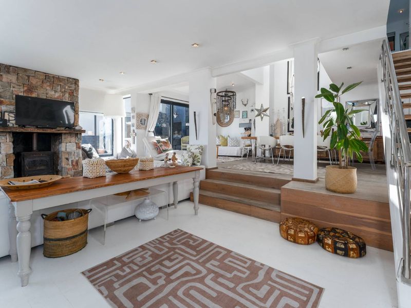 Spacious open-plan living and dining area featuring a striking stone fireplace, timber staircase, and split-level flooring with modern recessed lighting.