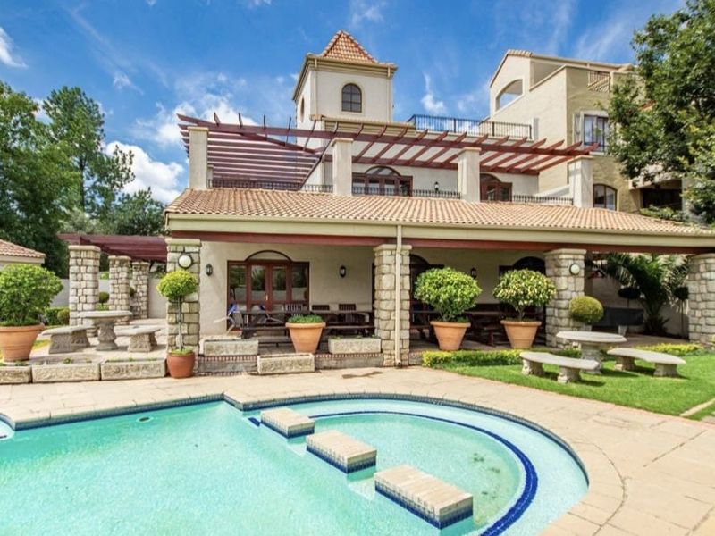 Spacious outdoor pool area featuring a covered patio with stone-clad pillars, a pergola, and integrated stone bench seating, perfect for entertaining.