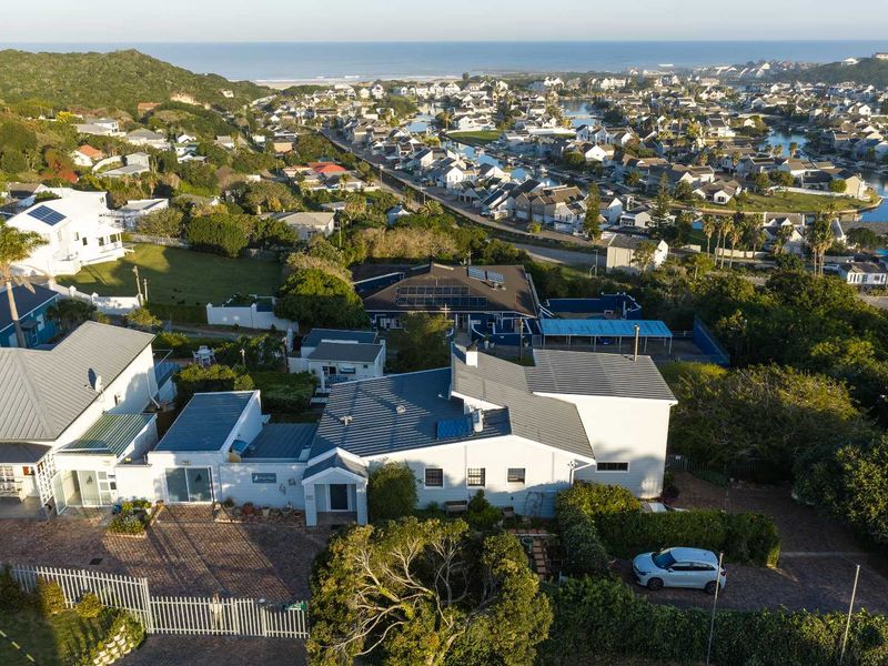 Aerial view of the property showcasing the roof structure, solar panels, paved driveway, and surrounding residential estate landscape.