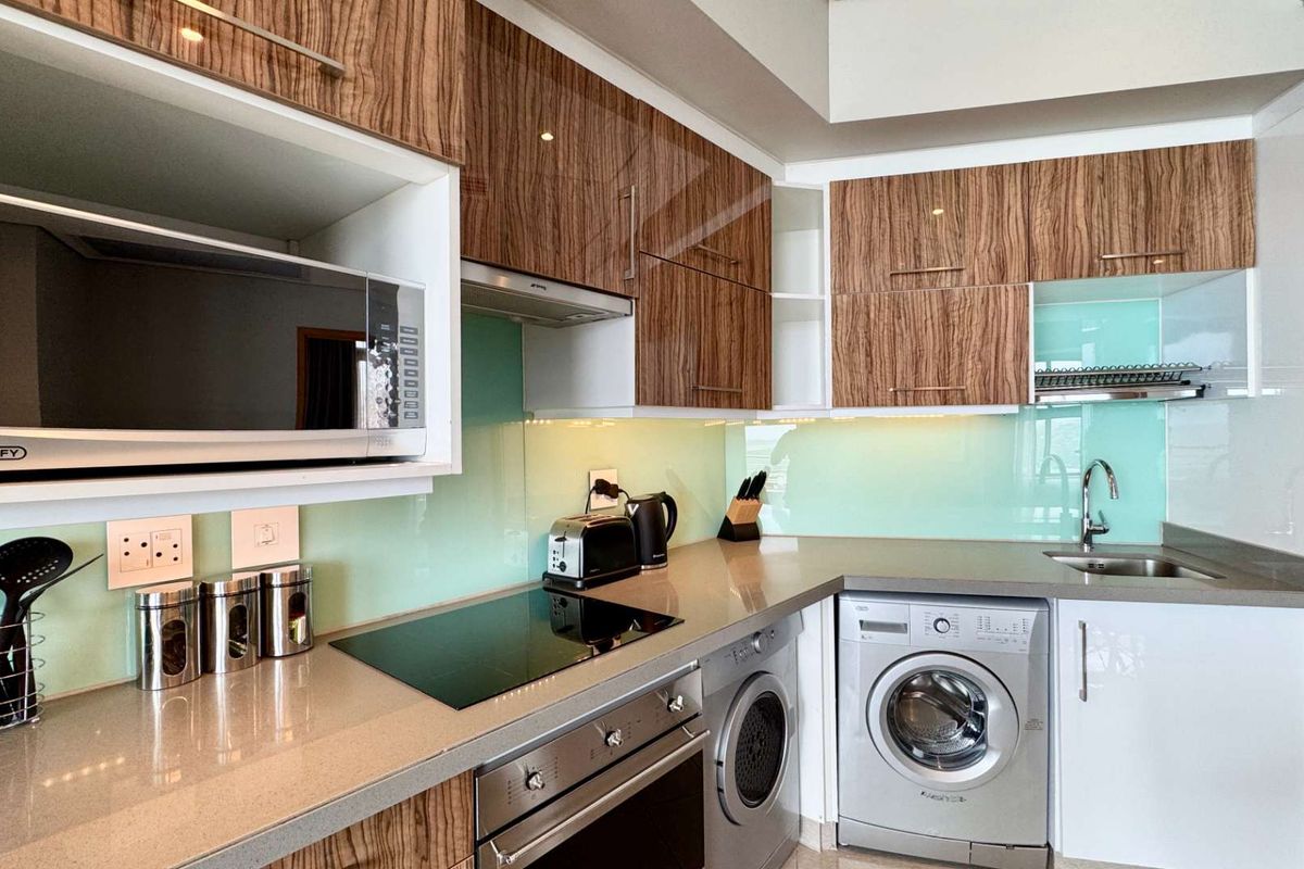 Modern kitchen featuring wood-grain cabinetry, stone countertops, a glass splashback, integrated oven, hob, extractor fan, and built-in microwave.