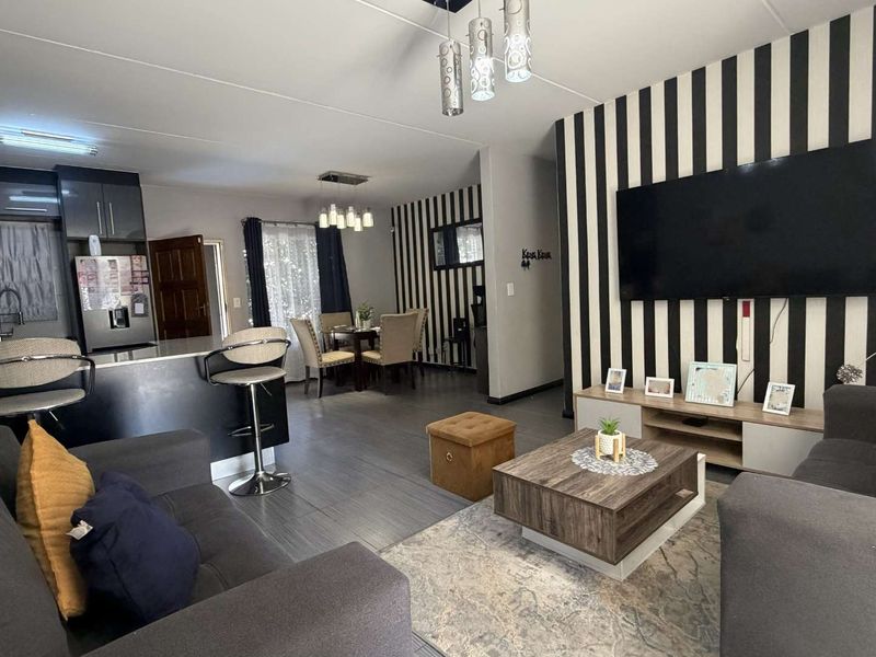 Open-plan living area featuring a modern kitchen with island, dining space, and lounge, finished with contemporary laminate flooring and integrated lighting.
