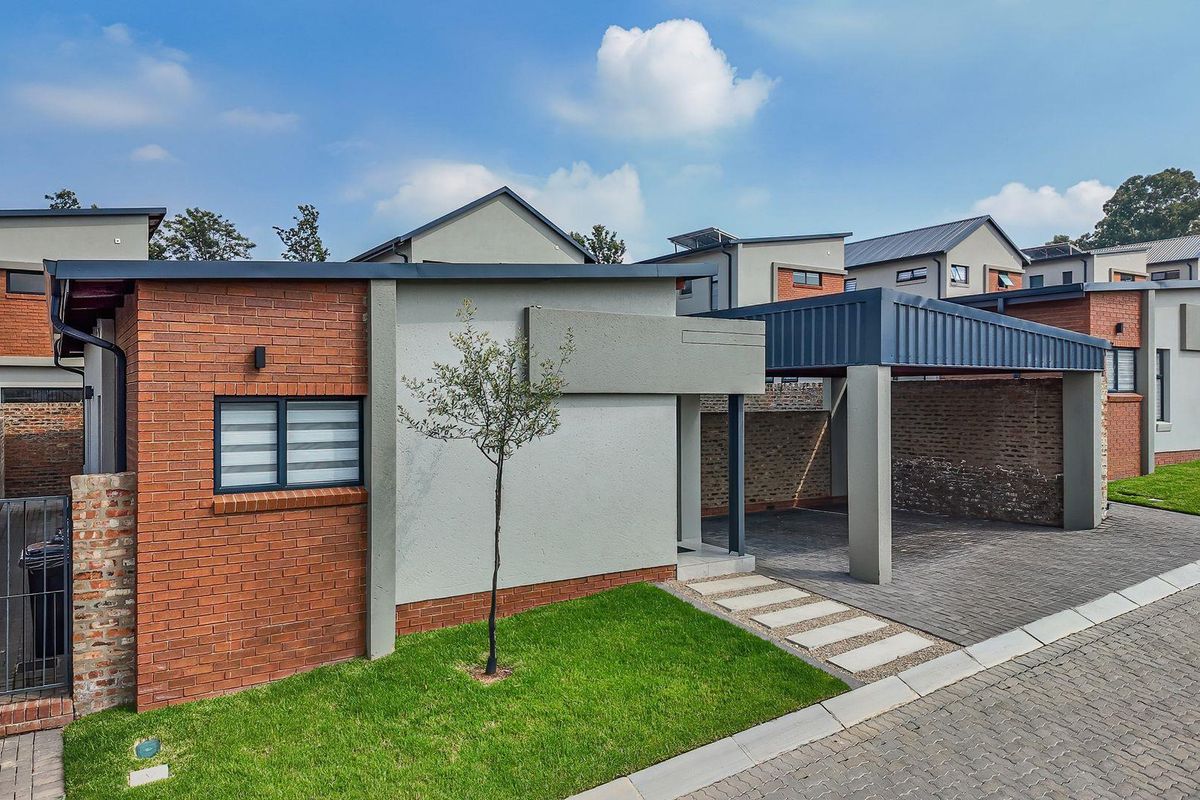 Modern cluster home exterior featuring a brick and plaster facade, a covered carport, and a neat paved driveway with a small front garden.