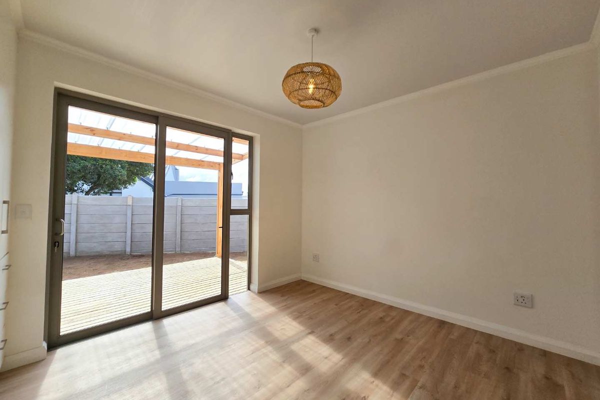 A bright, empty living room featuring light wood-look flooring, neutral walls, and large sliding glass doors that open onto a wooden patio.