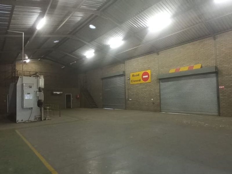 Spacious industrial warehouse featuring high ceilings with exposed steel trusses, concrete flooring, and multiple roller shutter doors for efficient access.