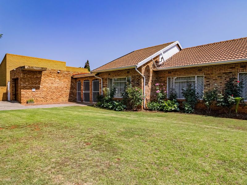 A well-maintained face brick house featuring a tiled roof, paved driveway, and a spacious front lawn with established garden beds.