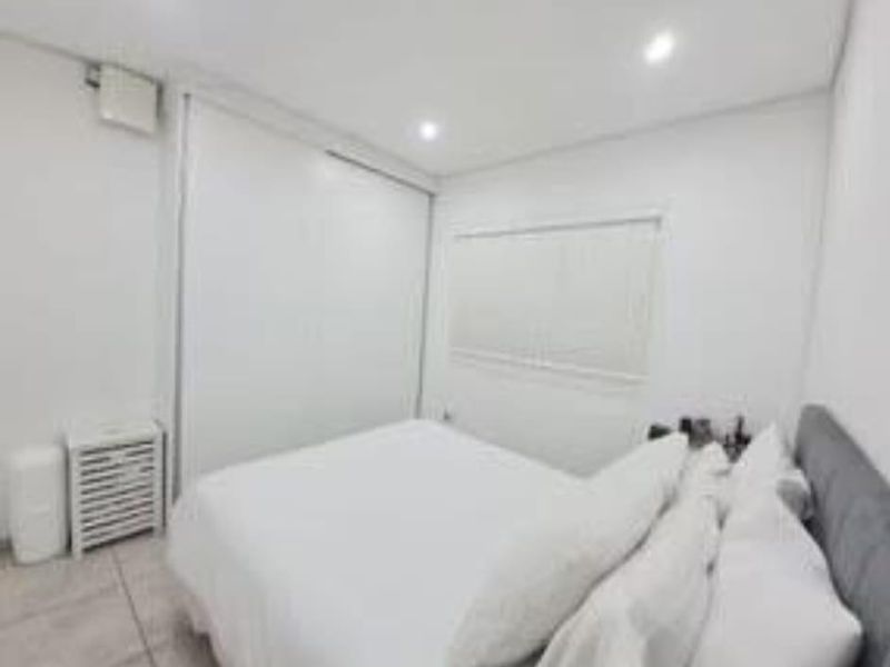 A bright bedroom featuring tiled flooring, recessed downlighting, and a built-in wardrobe with sliding doors.