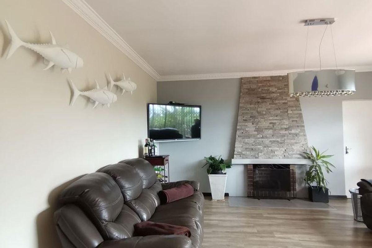 Spacious living room featuring a stone-clad fireplace, crown molding, and light-toned wood-look flooring.