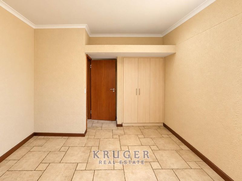 An empty bedroom featuring neutral tiled flooring, built-in cupboards, and a coved ceiling, providing a clean and versatile space.