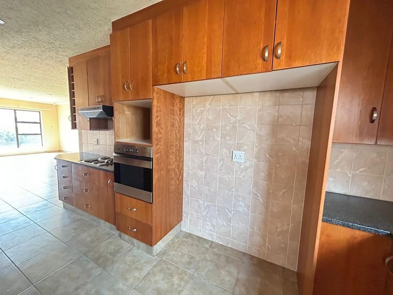 A functional kitchen featuring built-in wooden cabinetry, a built-in oven, hob, extractor fan, and tiled finishes, offering a clean and practical workspace.