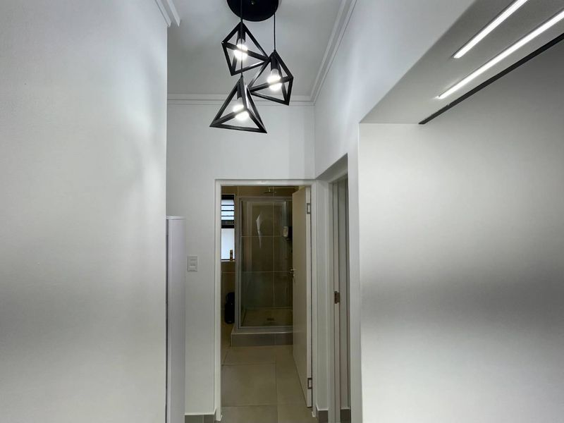 A clean, well-lit hallway featuring modern geometric pendant lighting and neutral tiled flooring, providing access to adjacent rooms.