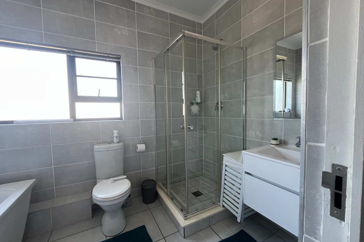 Modern bathroom featuring a glass shower enclosure, vanity cabinet with basin, toilet, and neutral grey wall and floor tiling.