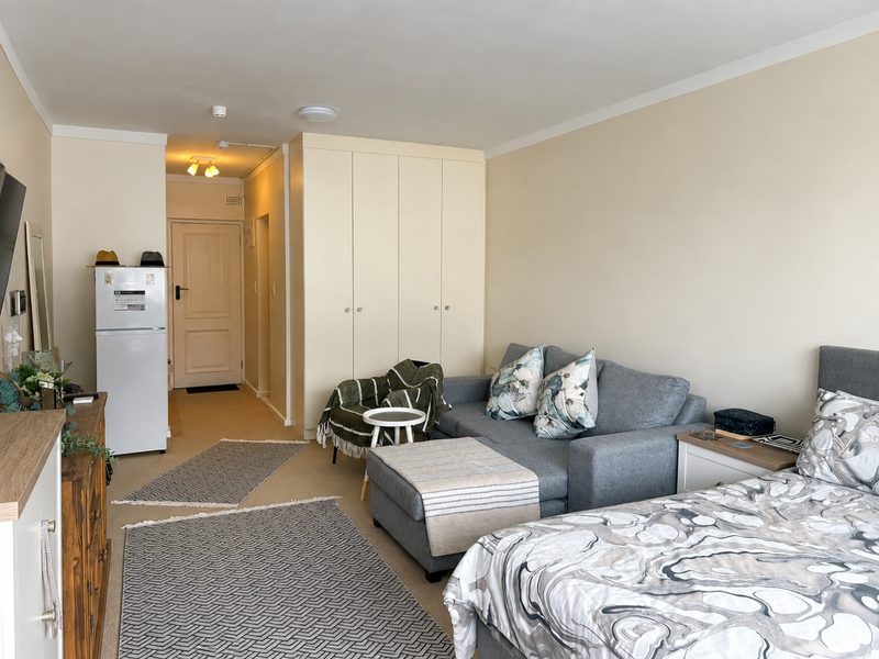 An open-plan studio apartment featuring neutral walls, carpeted flooring, and a large built-in wardrobe providing ample storage space.